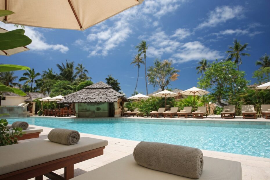 Luxury tropical resort pool with sun loungers palm trees and beach umbrellas on a clear sunny day