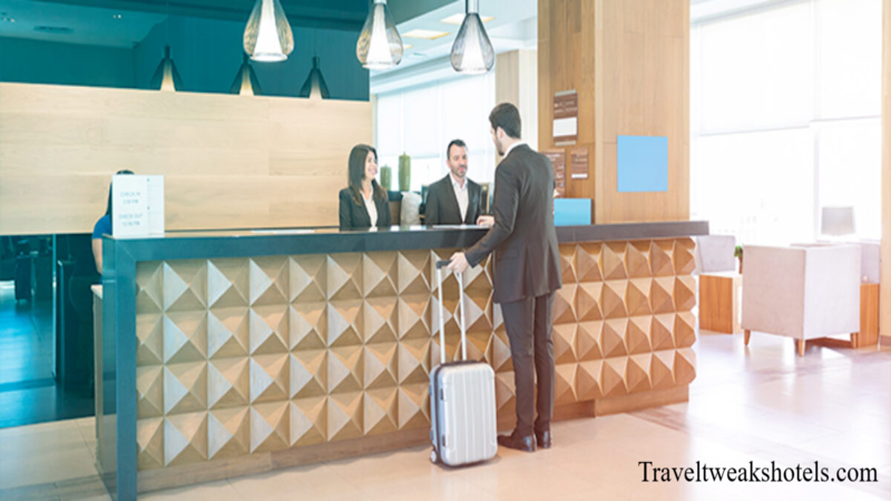 Business traveler checking in at a modern hotel reception desk with a suitcase while hotel staff assist at the front desk.